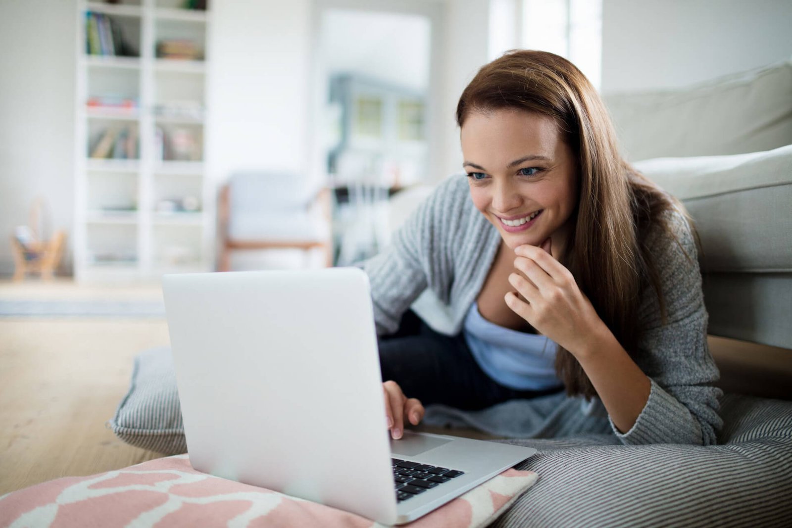 Frau liegt entspannt mit Laptop auf dem Sofa und nimmt am Online-Gruppenprogramm teil