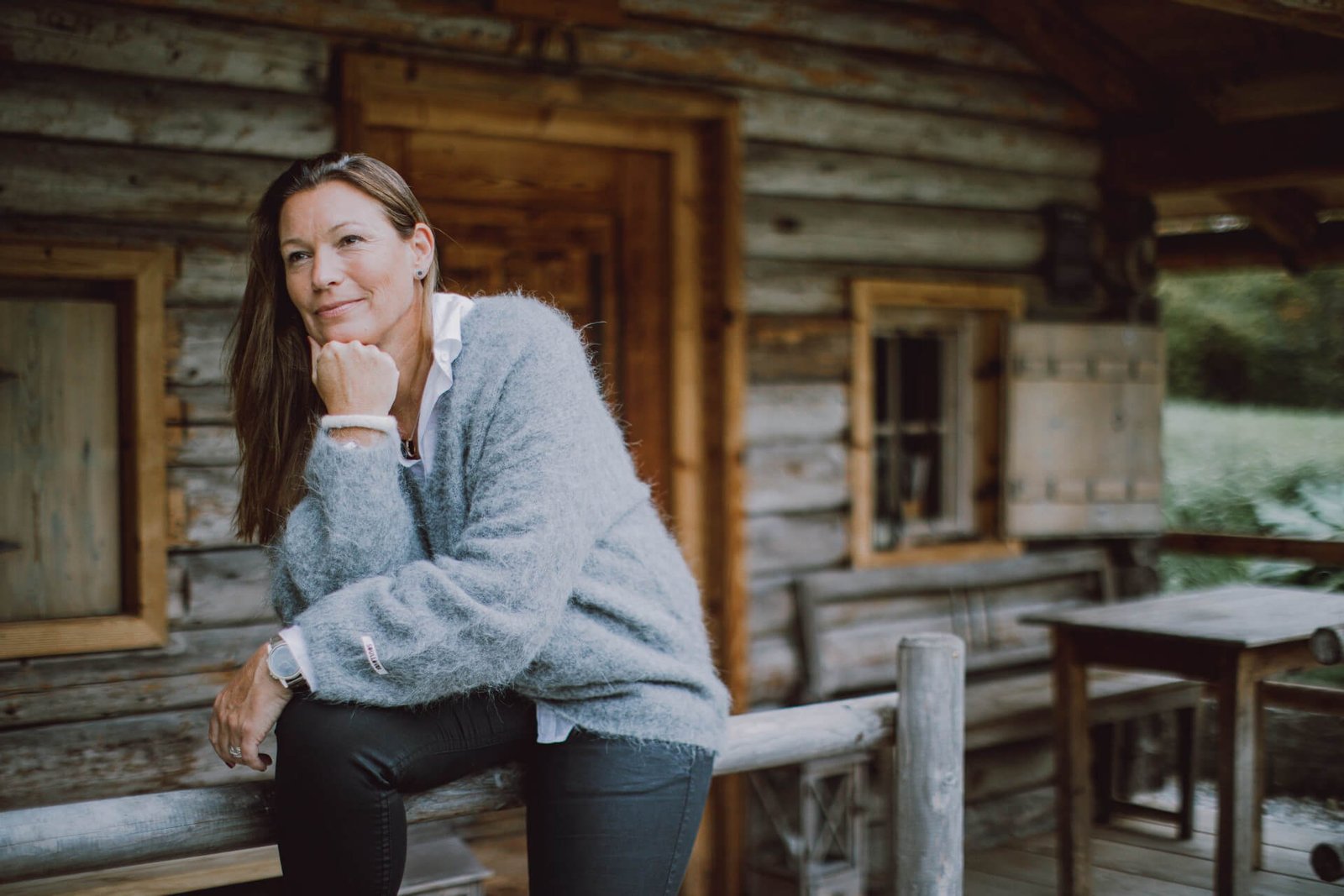 Carola Kissel sitzt nachdenklich vor einer Blockhütte im Wald