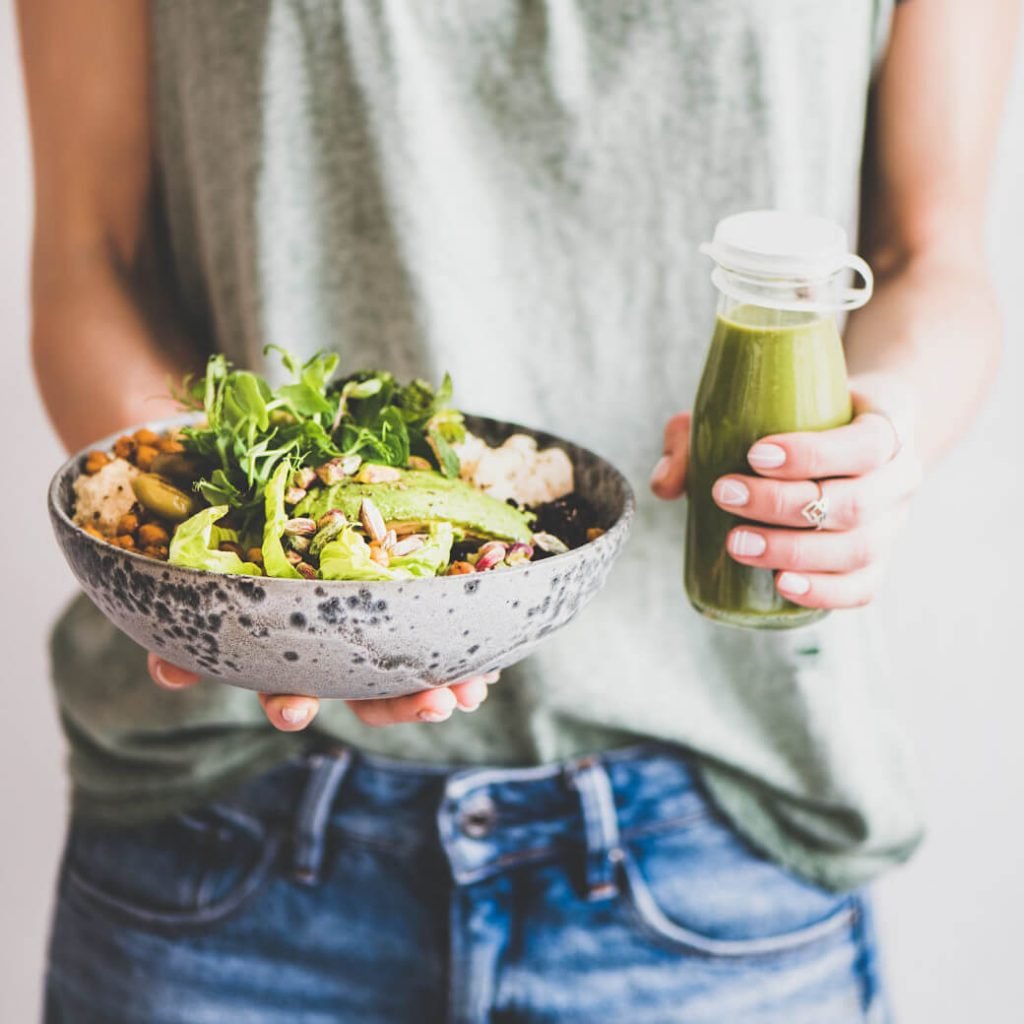 Frau hält eine Bowl mit Salat und Kichererbsen und eine Flasche grünen Smoothie